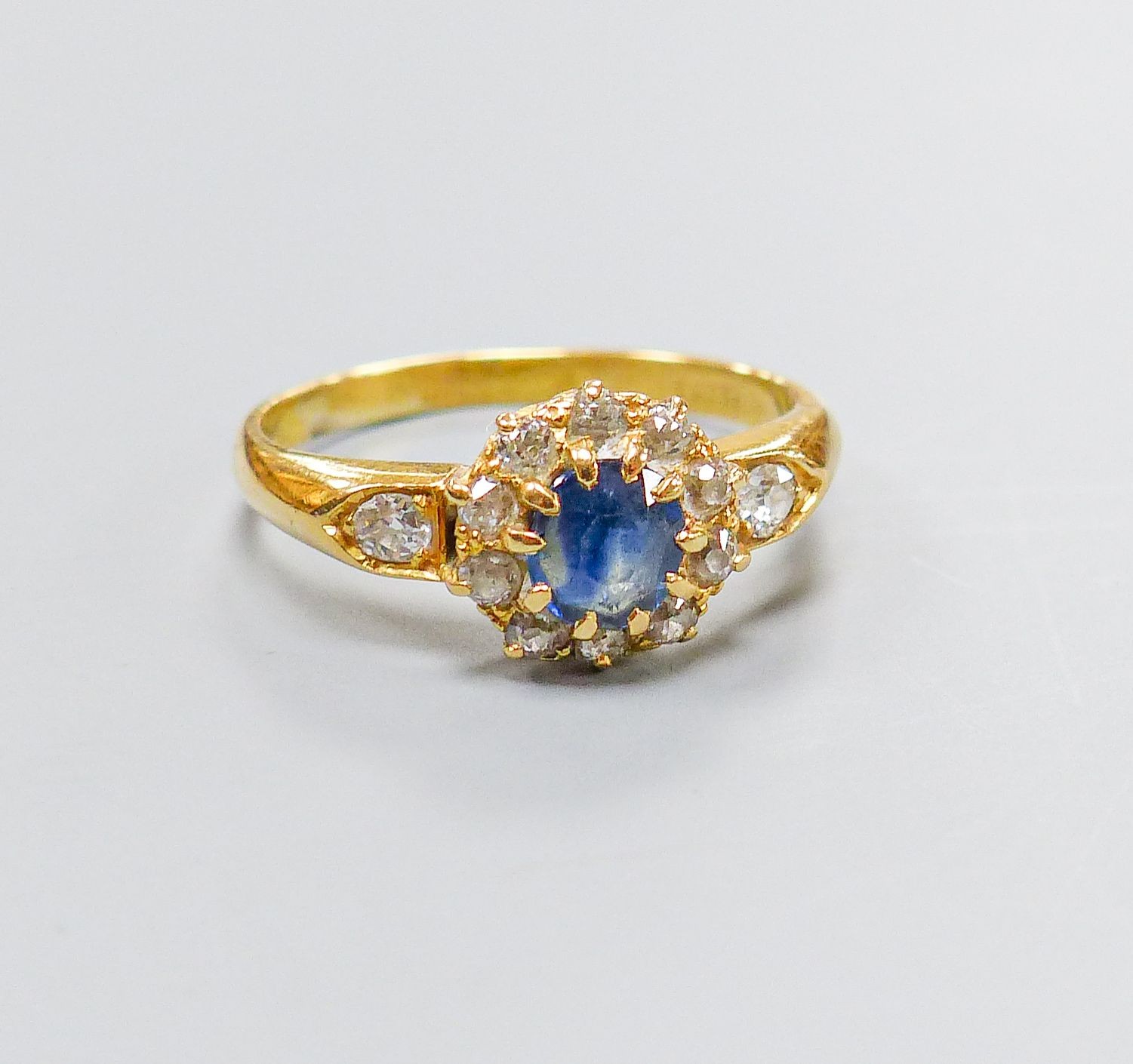 An 18ct, sapphire and diamond set circular cluster ring, with diamond set shoulders, size M, gross 3.4 grams.